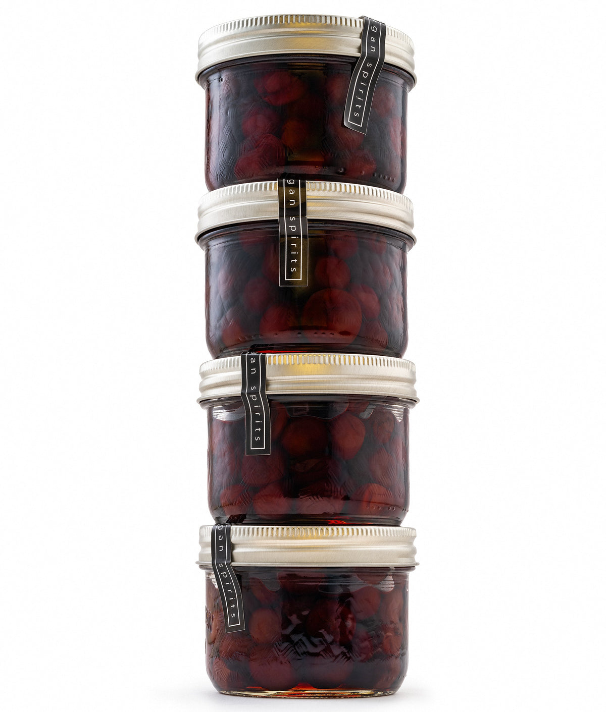 Four stacked glass jars filled with dark re drunken sour cherries, each with a silver metal lid and a black-and-gold vertical label, isolated on a white background.