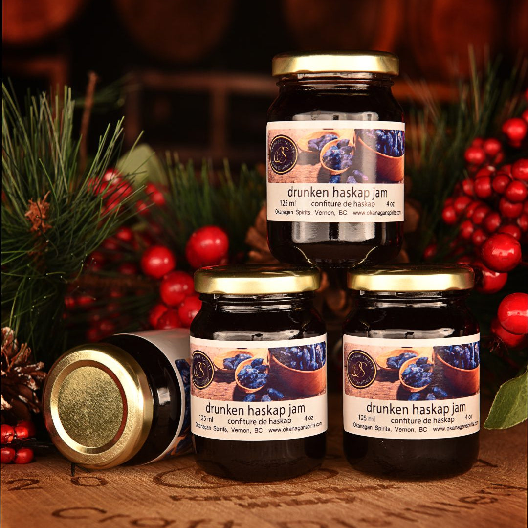 Three jars of 'drunken haskap jam' with decorative elements on a wooden surface.