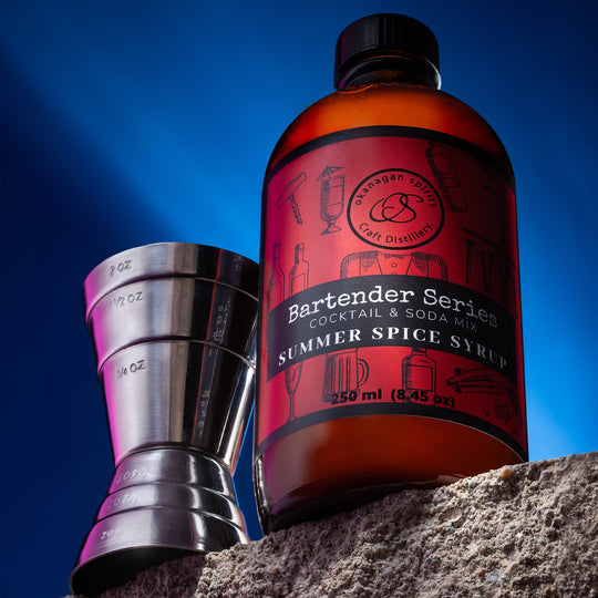 Bottle of Summer Spice Syrup with a jigger on a stone surface against a blue sky