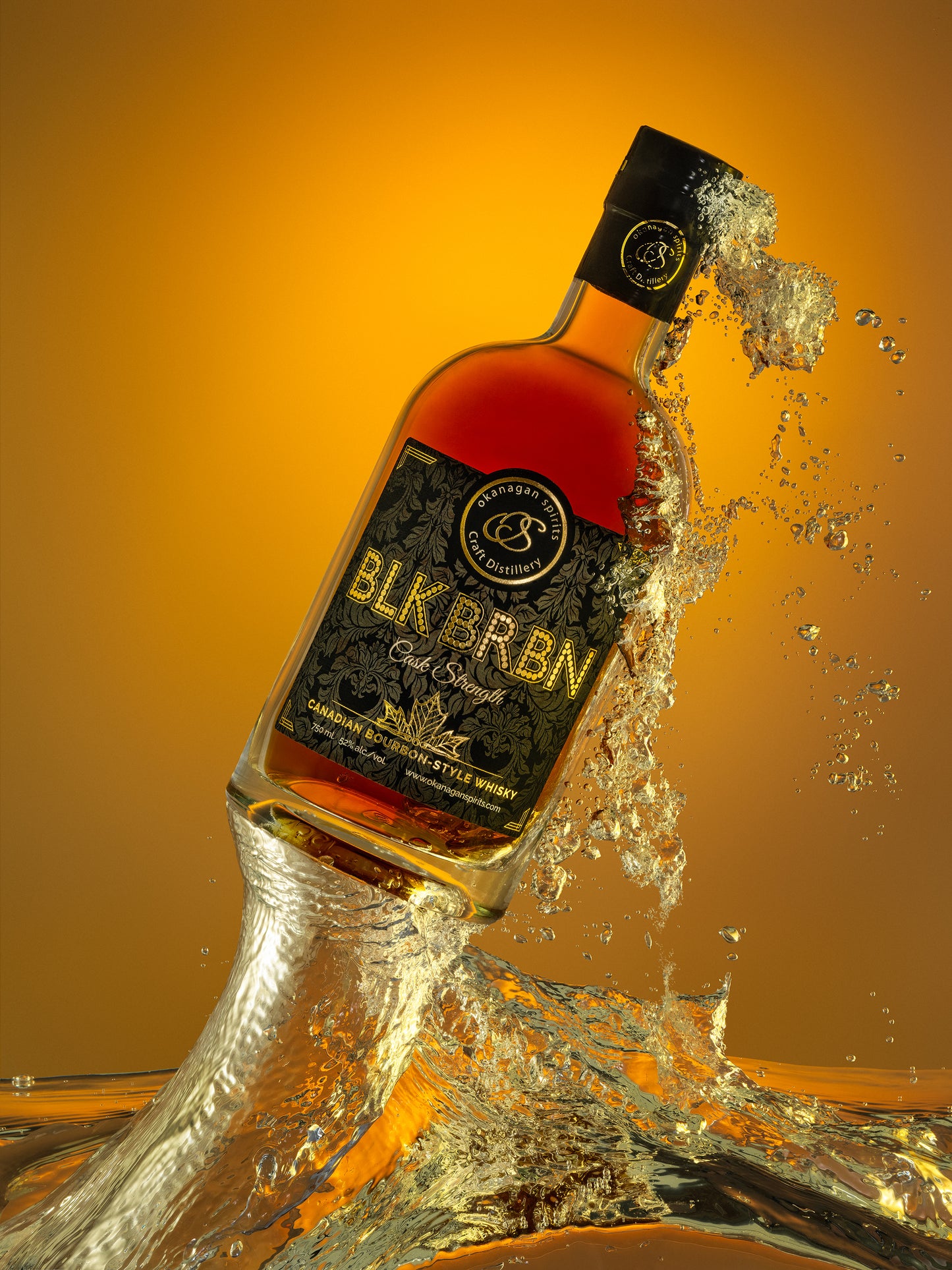 A bottle of Blk Brkn Bourbon-Style Canadian Whisky is shown tilted with a dramatic splash of clear liquid and water around it against a warm orange gradient background.