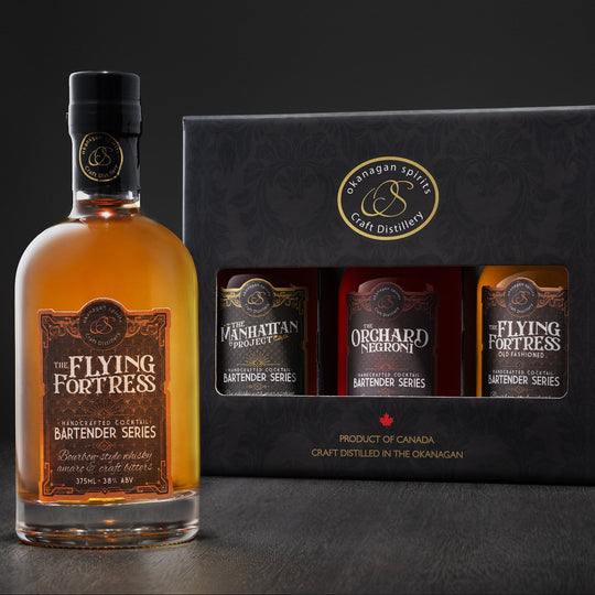 A bottle of The Flying Fortress Bartender Series Old Fashioned Pre-batched cocktail alongside its black gift box containing three Mickey sized bottles: Manhattan, Negroni, and the Flying Fortress Old Fashioned. The products are shown on a dark studio background.