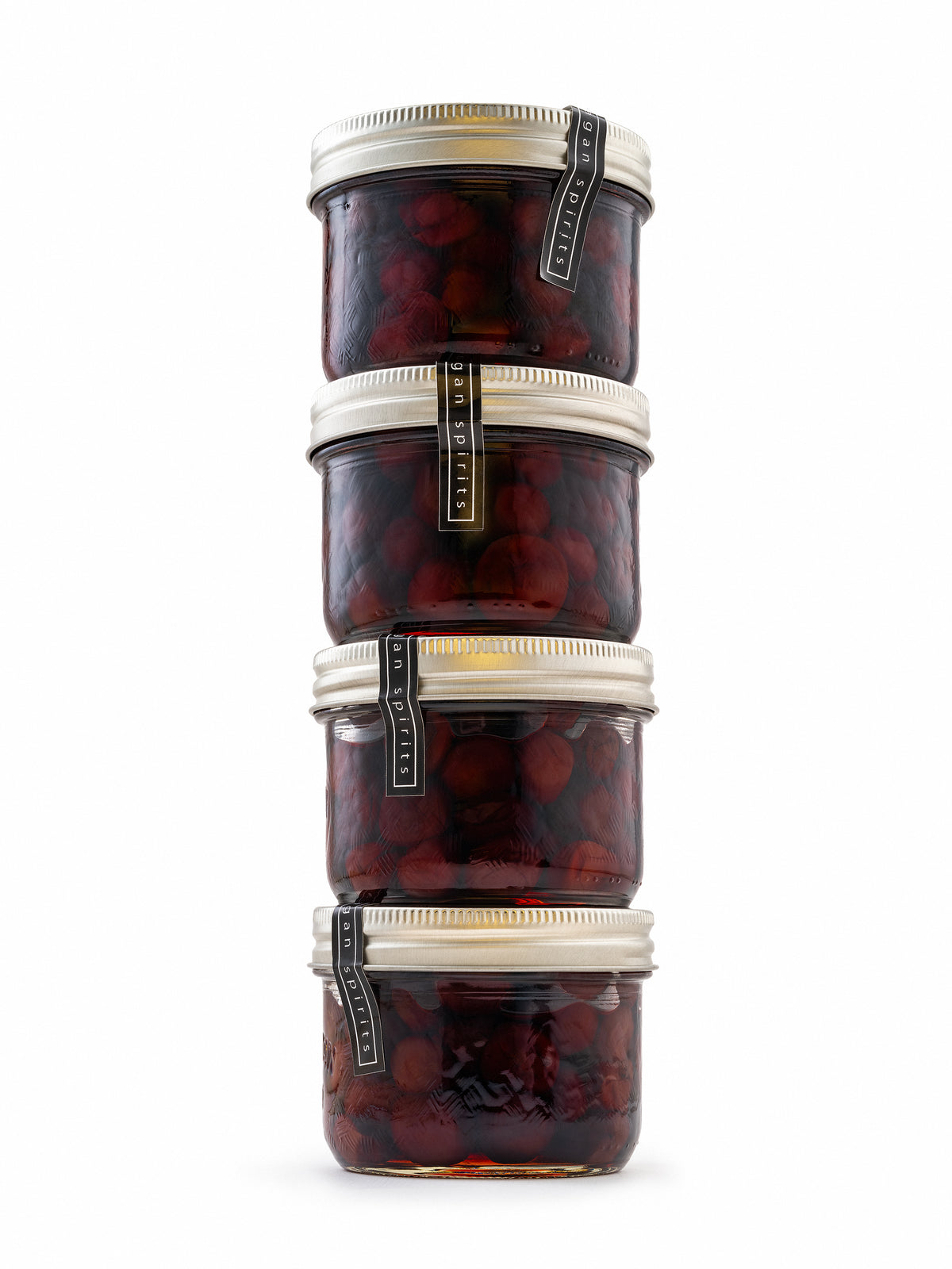 Four stacked glass jars filled with dark re drunken sour cherries, each with a silver metal lid and a black-and-gold vertical label, isolated on a white background.