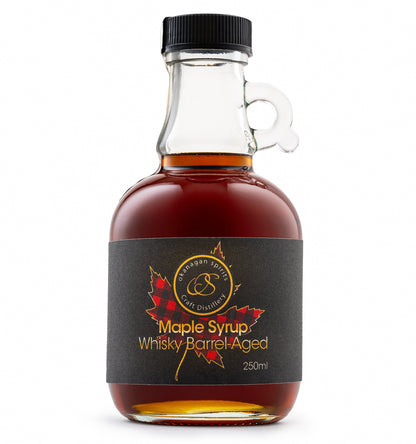 A 250ml bottle of Barrel Aged maple syrup by Okanagan Spirits, featuring amber liquid in a clear glass bottle with a black cap and a black label with red maple leaf graphics.