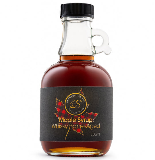 A 250ml bottle of Barrel Aged maple syrup by Okanagan Spirits, featuring amber liquid in a clear glass bottle with a black cap and a black label with red maple leaf graphics.