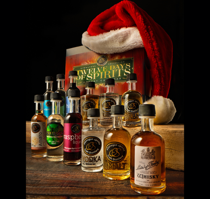 A collection of assorted liquor bottles arranged in front of a large gift box, with a red Santa hat resting behind them against a black background. The front bottle labels include Laird of Fintry Single Malt, Family Reserve Vodka and Raspberry Liqueur.
